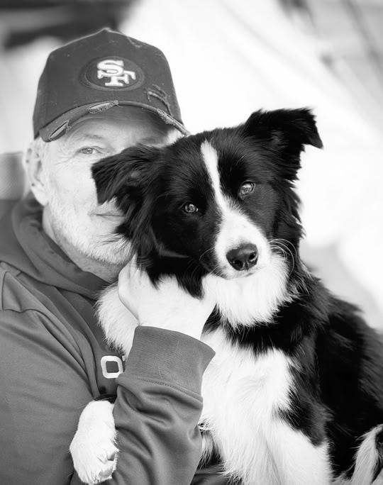 Eine Person mit Baseballkappe hält einen schwarz-weißen Hund.